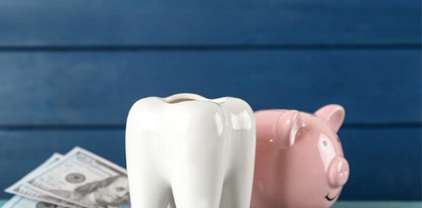 A ceramic model of a tooth, a piggy bank, and money on a light blue wooden table