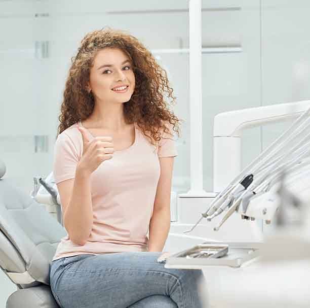 Female dental patient in pink shirt giving thumbs up